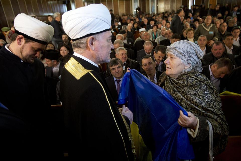An elderly woman holds a Ukrainian flag in front of Russia's top Muslim Cleric Ravil Gainutdin, center, during the Crimean Tatar Qurultay, a religious congress, in Bakhchysarai, Crimea, Saturday, March 29, 2014. The Crimean Tatar Qurultay, a religious congress will determine whether the Tatars will accept Russian citizenship and the political system that comes with it, or remain Ukrainian citizens on Russian soil. (AP Photo/Pavel Golovkin)