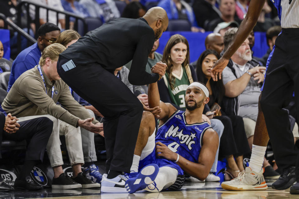 Orlando Magic coach Jamahl Mosley helps guard Jalen Suggs (4) off the floor after Suggs was fouled by the Milwaukee Bucks during the second half of an NBA basketball game Saturday, Nov. 11, 2023, in Orlando, Fla. (AP Photo/Kevin Kolczynski)