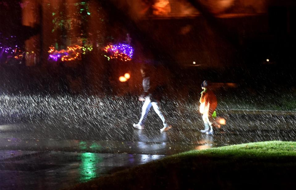 Some trick-or-treaters in Monroe Township, Michigan, were met with snow on Oct. 31, 2023. Car headlights illuminate falling snow and trick-or-treaters as this image was taken through glass for better image effectiveness.