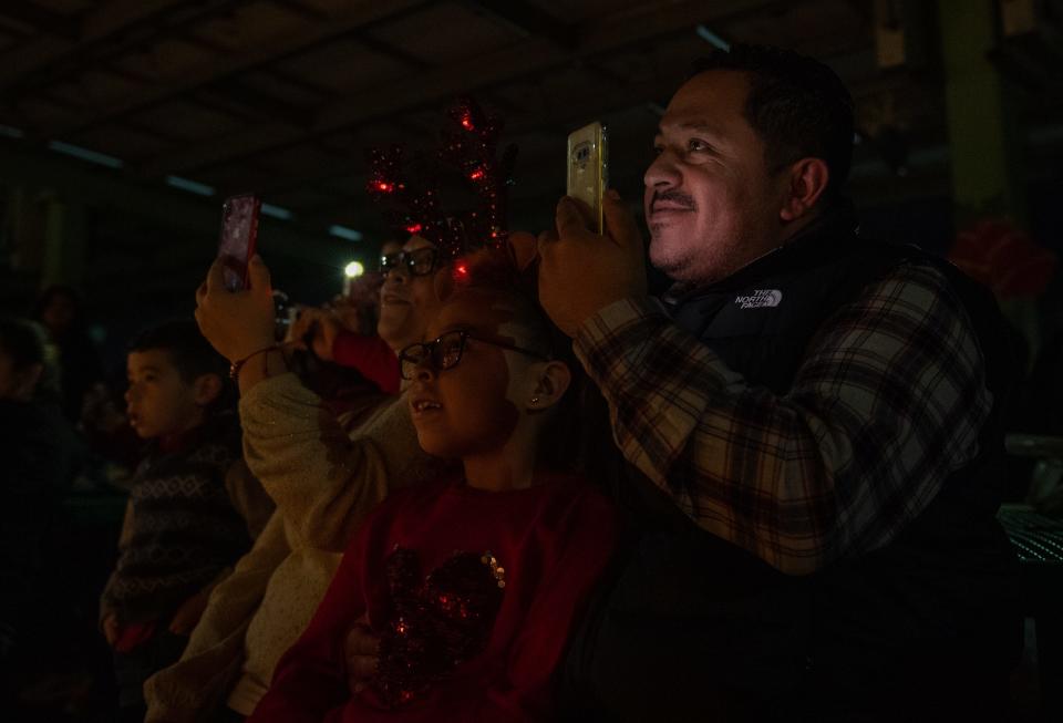 A dad hugs his daughter with one hand as he records the performance with his other hand during the Boronda Meadows Elementary School annual Posada Night on Dec. 11, 2019.