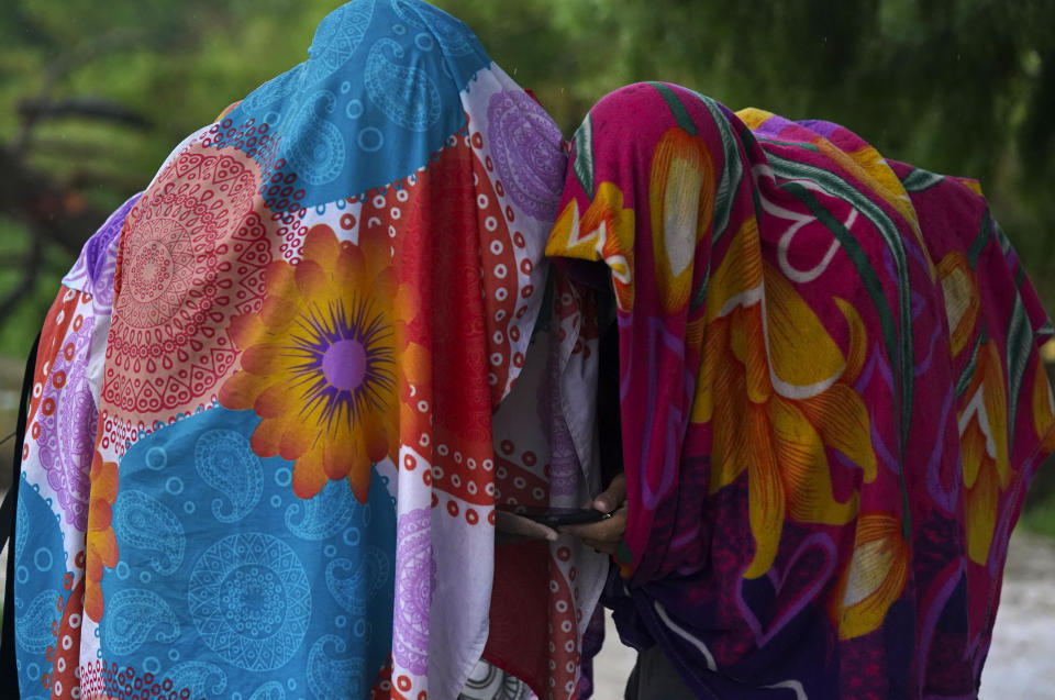 FILE-Venezuelan migrants, using a wrap and a towel, respectively, as protection from the rain, consult the CBPOne app, on the banks of the Rio Grande, in Matamoros, Mexico, Saturday, May 13, 2023. Asylum-seekers say joy over the end of the public health restriction known as Title 42 this month is turning into anguish with the realization of how the Biden administration's new rules affect them. Though the government opened some new avenues for immigration, many people's fate is largely left up to a U.S. government app that is limited and unable to decipher and prioritize human suffering and personal risk. (AP Photo/Fernando Llano)