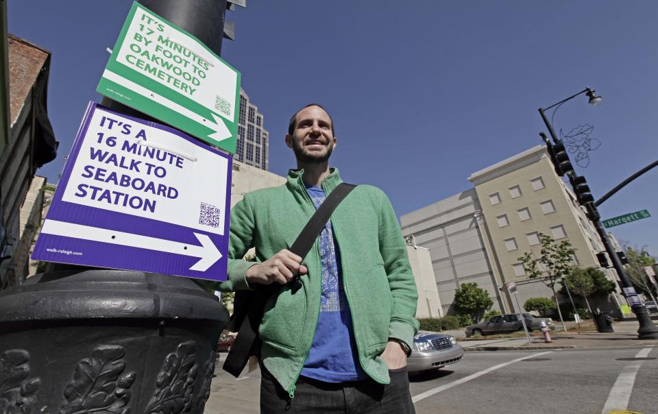 CORRECTS SPELLING OF TOMASULO - Matt Tomasulo poses for a photo by some of his signs in downtown Raleigh, N.C., Wednesday, April 11, 2012. On a January night he and friends put up 27 signs that advised people how to walk to various locations. The project, part of his master's thesis, has taken off with city officials, with two other states now planning to use his signs. (AP Photo/Gerry Broome)