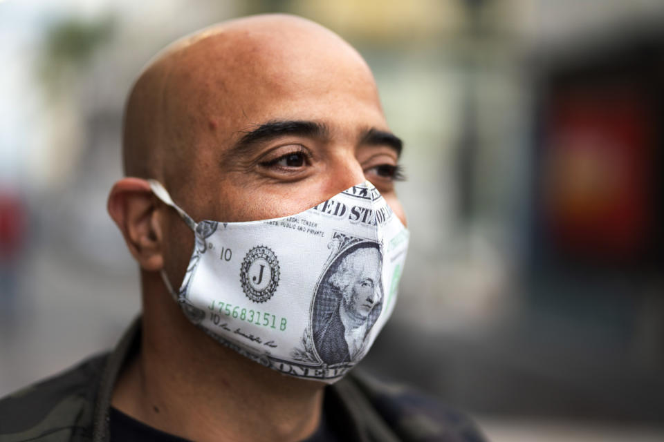 A man whose mask features U.S. dollar bills stands in line for free food from residents helping others facing economic hardship amid the lockdown to contain the spread of COVID-19 in the financial district of Montevideo, Uruguay, Saturday, April 25, 2020. (AP Photo/Matilde Campodonico)