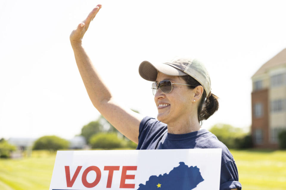  Julia Turner of Bowling Green waves to drivers holding a sign for a local candidate in Bowling Green on Tuesday, May 21, 2024. (Kentucky Lantern photo by Austin Anthony)