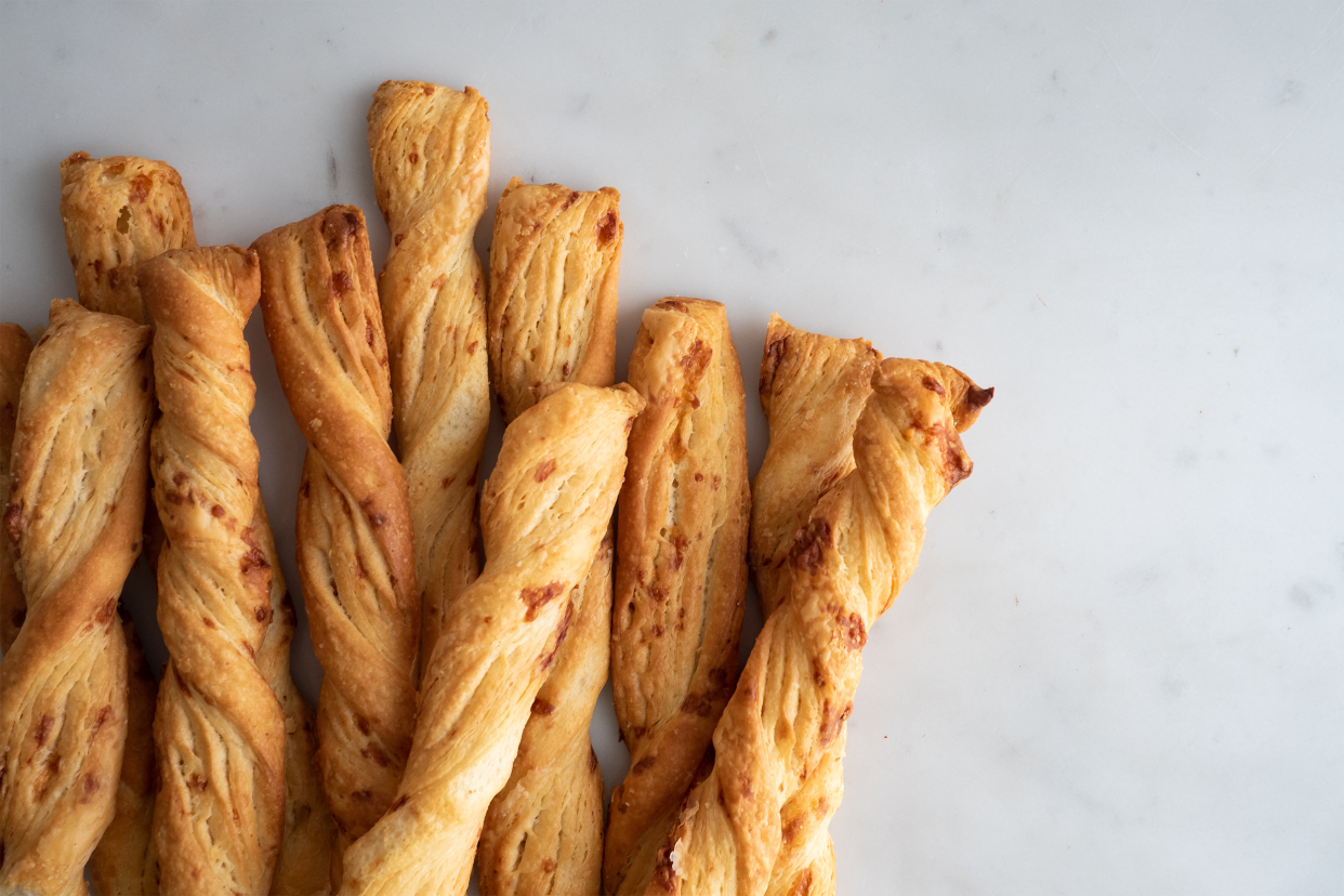 Closeup of nine cheese straws on the left side and middle of a slab of marble