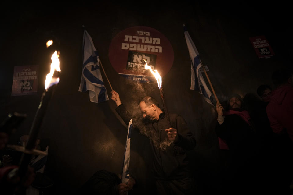 Israeli demonstrators hold torches during a protest against the government's plans to overhaul the country's legal system, in Tel Aviv, Israel, Saturday, Jan. 14, 2023. Tens of thousands of Israelis have gathered in central Tel Aviv to protest plans by Prime Minister Benjamin Netanyahu's new government to overhaul the country's legal system and weaken the Supreme Court. (AP Photo/Oded Balilty)