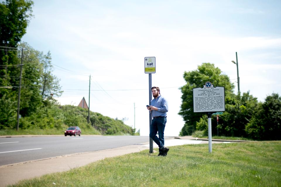 Downtown reporter Ryan Wilusz checks his phone for the arrival time of a bus while waiting at a stop on Western Avenue in Knoxville, Tennessee, on April 30, 2019.