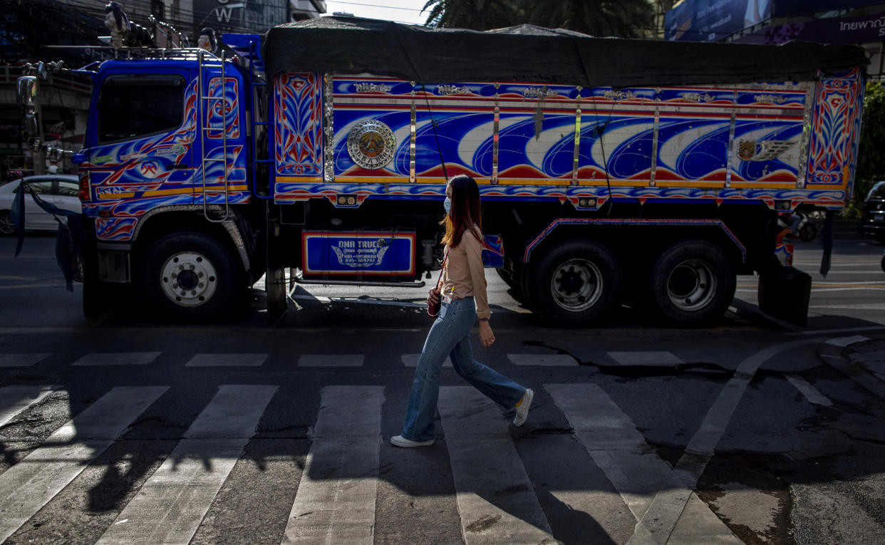 A woman, wearing a face mask, walks in the foreground of a truck in Bangkok, Thailand, Wednesday, May 13, 2020. Thai government continue to ease restrictions related to running business in capital Bangkok that were imposed weeks ago to combat the spread of COVID-19. (AP Photo/Gemunu Amarasinghe)