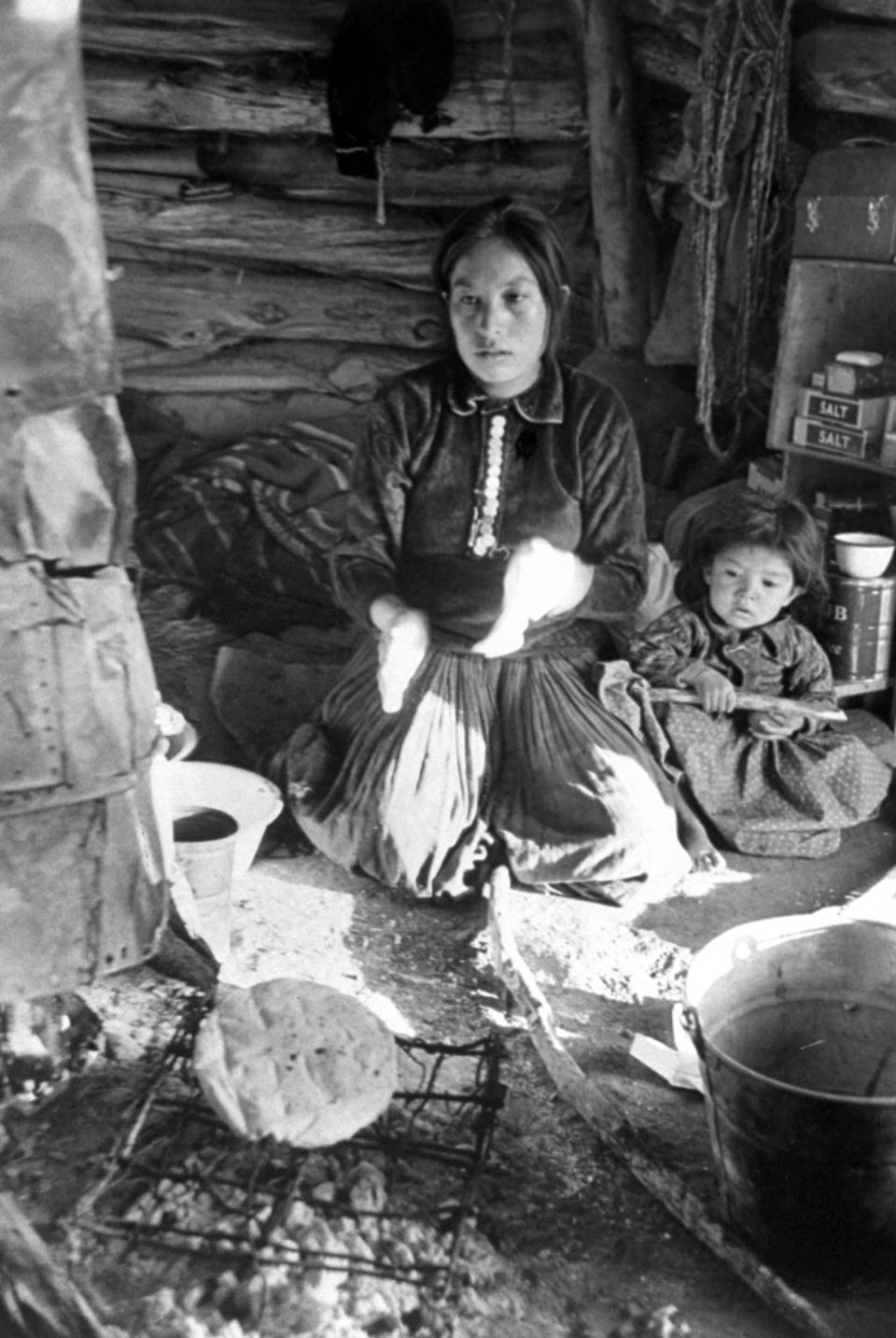 <b>Caption from LIFE.</b> Baking bread, a woman kneels by the fire while loaf cooks on crude metal grill. This native bread is a major item of Navajo diet.