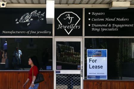 A woman walks past a former jewellery store displaying a "For Lease" sign in a window in the Western Australian capital city of Perth March 5, 2015. REUTERS/David Gray