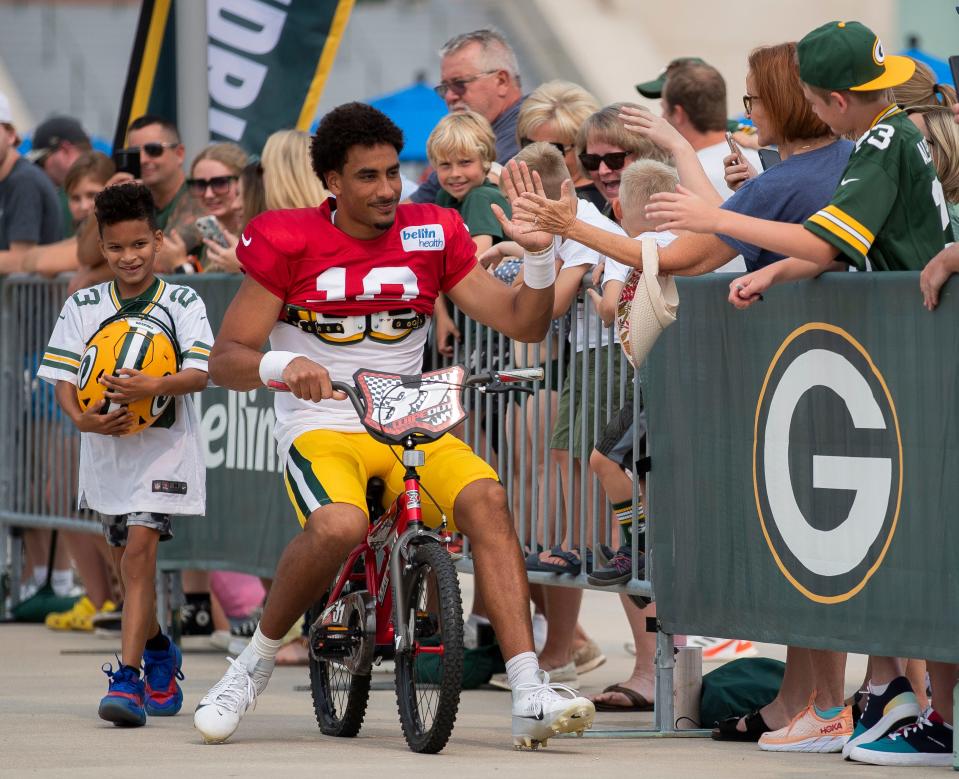 Packers quarterback Jordan Love slaps hands with fans as he rides past on a bicycle before practice Aug. 1 at Lambeau Field in Green Bay.