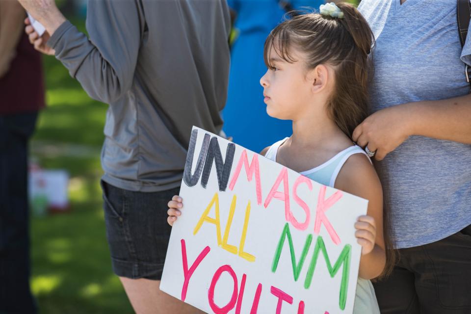 A child stands among those asking for the state to lift mask restrictions for youth on June 26.