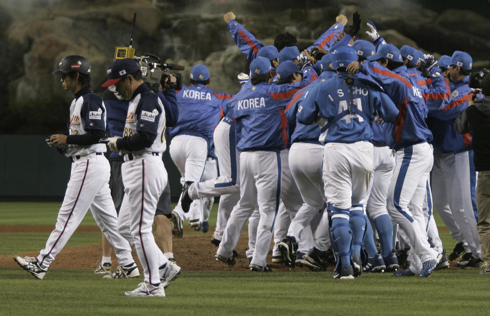 FILE- Team Japan's Tomoya Satozaki, left, walks off the field with a coach as Team South Korea celebrates their 2-1 win over Japan on March 15, 2006 at Angel Stadium in Anaheim, Calif.. in the 2nd round of the World Baseball Classic. (AP Photo/Ted S. Warren, File)