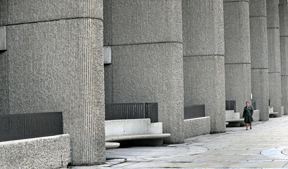 A woman walks outside of the Charles F. Hurley Building, which features a distinct corduroy concrete exterior.