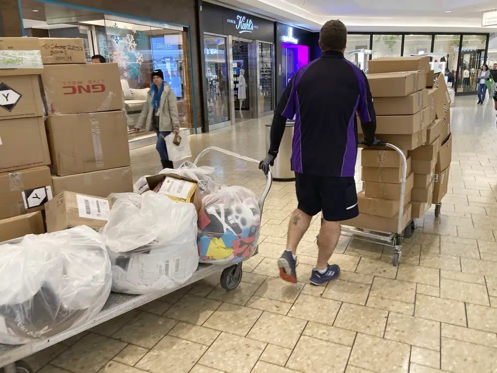 A FedEx delivery person guides carts of packages to stores in Cherry Creek Mall Wednesday, Nov. 30, 2022, in Denver. (AP Photo/David Zalubowski, File)