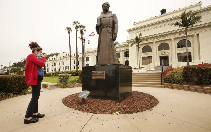 VENTURA, CA - JUNE 24: Erica Cohee from Thousand Oaks photographs the bronze statue of Father Junipero Serra who founded nine Spanish missions in California including Mission San Buenaventura as it stands in front of Ventura City Hall. A joint statement was issued from local political, indigenous and Catholic leaders pledging to remove the monument, originally commissioned in the 1930s but replaced in 1989. "The time has come for the statue to be taken down and moved to a more appropriate nonpublic location," read the statement, issued by Ventura Mayor Matt LaVere. After a protest last weekend Ventura city spokeswoman Heather Sumagaysay said the city is making plans to host community discussions regarding the Serra statue and there is no timeline for its removal, she said. "It is our priority to be receptive to public concerns and provide an environment where all voices are heard and respected. A historic decision such as this will involve the voices of the Chumash tribe, the City Council and the residents of Ventura," Sumagaysay said in an emailed statement. "The city remains committed to collaborating with the community to determine next steps. We will inform the public of opportunities to participate and offer input at a future meeting." The move comes after a Father Serra statue was toppled last weekend on Olvera St. in downtown Los Angeles and people were considering changing the name of Ft Bragg, but voted the change down. Ventura City Hall on Wednesday, June 24, 2020 in Ventura, CA. (Al Seib / Los Angeles Times)