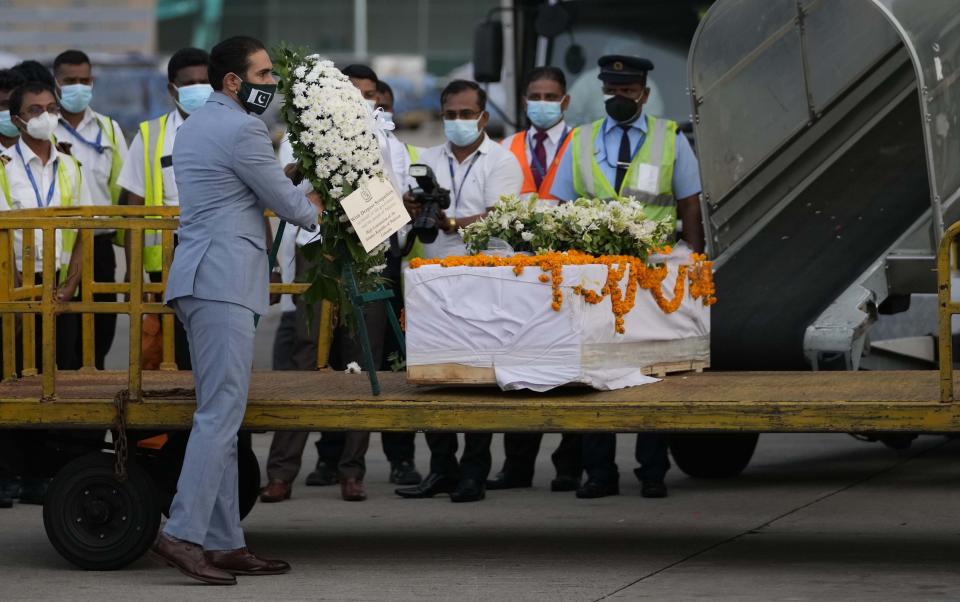 An unidentified Pakistani diplomatic official places wreath of flowers at the remains of Priyantha Kumara, a Sri Lankan employee who was lynched by a Muslim mob in Sialkot last week, after it was unloaded at an air port in Colombo, Sri Lanka, Monday, Dec. 6, 2021. (AP Photo/Eranga Jayawardena)