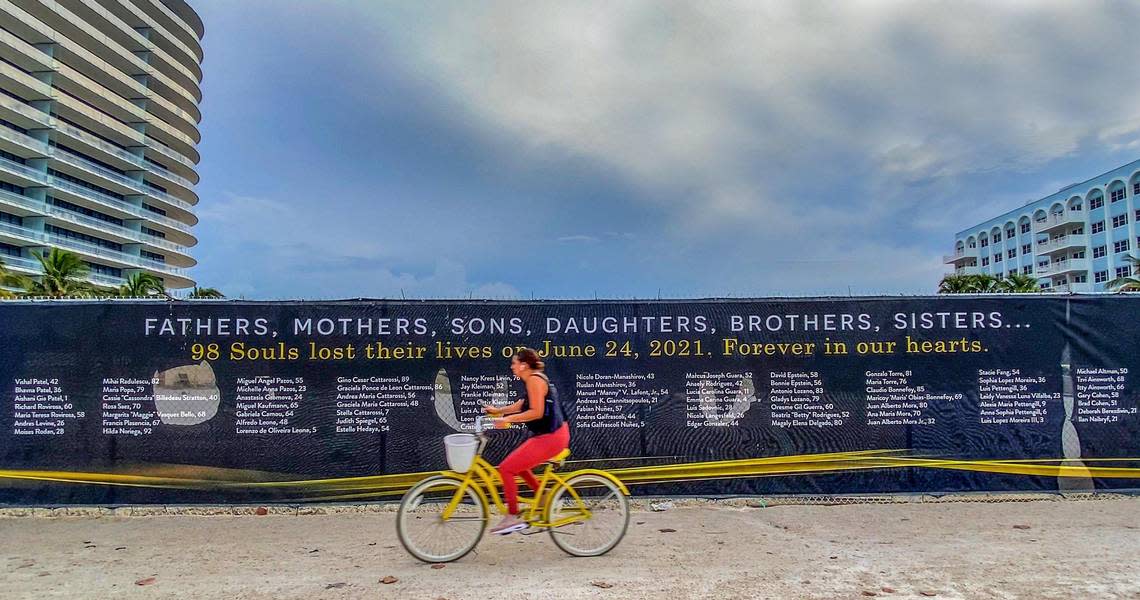 A woman bikes by a banner that honors the 98 victims of the Champlain Towers South condominium building collapse.
