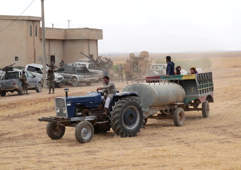 Civilians ride on a tractor past Turkey-backed Syrian rebel fighters as they withdraw from the border town of Tal Abyad