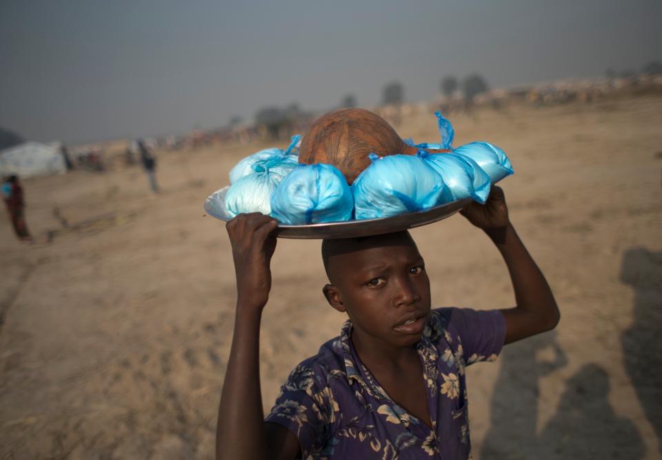 A boy carries bags of corn meal to sell, inside an informal camp housing an estimated 100,000 displaced people, at Mpoko Airport in Bangui, Central African Republic, Wednesday, Jan. 8, 2014. Food and supplies distribution by the World Food Program and the United Nations Refugee Agency began Tuesday and was expected to last 10 days. It is the first aid delivery to reach the camp since Dec. 15, and many families were lacking food or even rudimentary shelter from the harsh daytime sun and chilly nights. Residents were receiving supplies including rice, cooking oil, tarps, mats, and blankets. (AP Photo/Rebecca Blackwell)