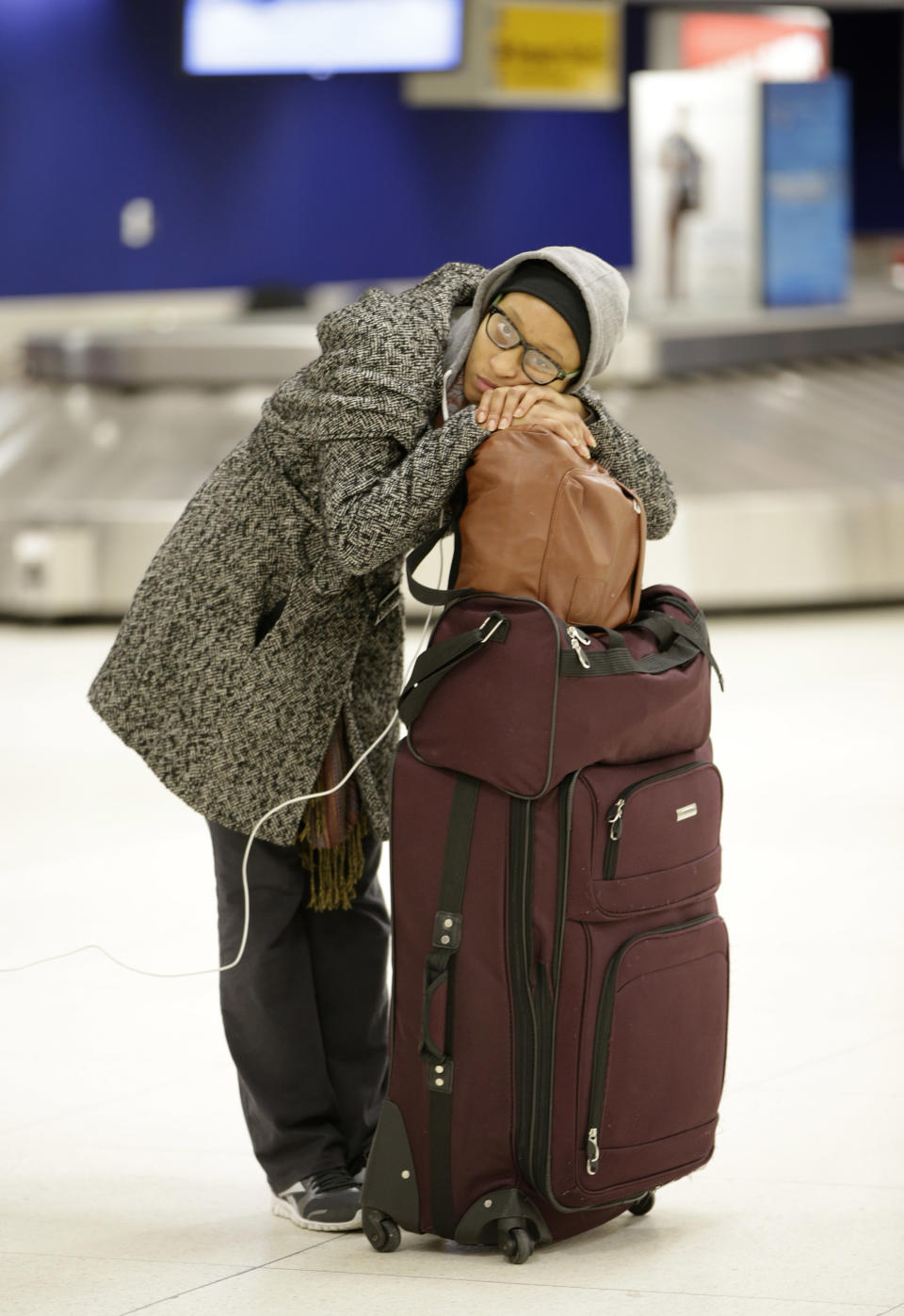 A woman, who did not want to be identified, rests on her luggage as she waits in the baggage area of Terminal 2 at Kennedy International Airport after a Delta flight from Toronto to New York skidded off the runway into a snow bank, temporarily halting all airport flights, Sunday, Jan. 5, 2014, in New York. (AP Photo/Kathy Willens)