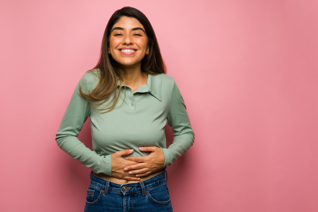 The food was delicious. Satisfied young woman smiling and rubbing her full stomach after eating lunch