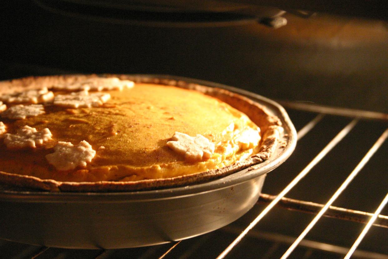 Appetizing pumpkin pie with maple leaf decor in oven.