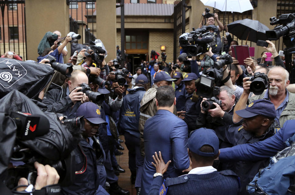 Carl Pistorius, at center in blue suit, the brother of Oscar Pistorius is escorted by police as he arrives at the high court in Pretoria, South Africa, Monday, March 3, 2014. Oscar Pistorius is charged with murder with premeditation in the shooting death of girlfriend Reeva Steenkamp in the pre-dawn hours of Valentine's Day 2013. (AP Photo/Schalk van Zuydam)