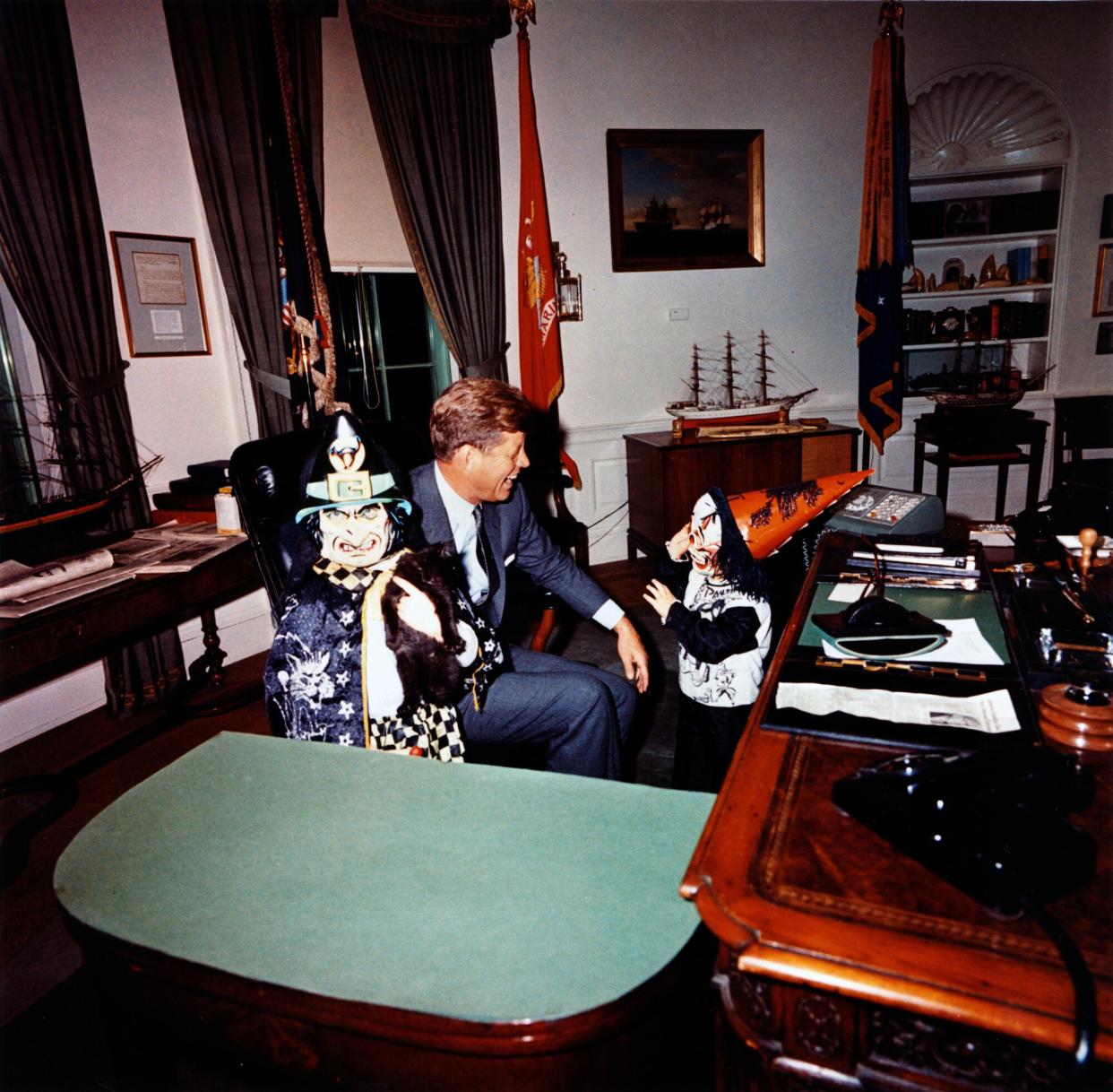 This photograph by Cecil Stoughton shows Caroline Kennedy and John F. Kennedy, Jr. visiting President John F. Kennedy in the Oval Office on Halloween in their costumes.