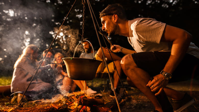 Person tasting food from campfire pot