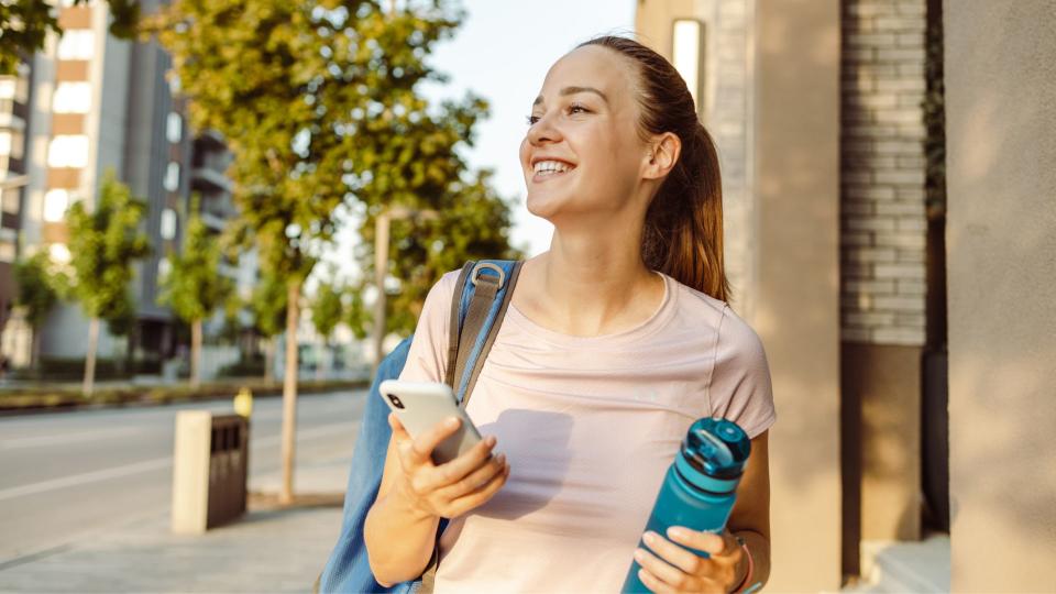 Woman holding gym bag and water bottle walking into the gym