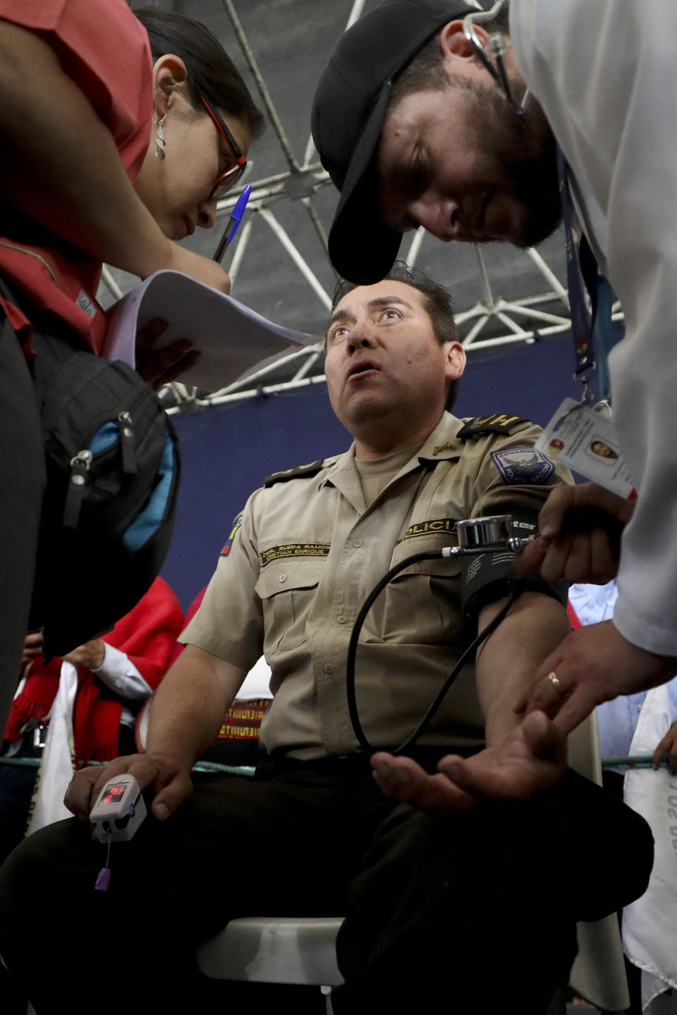 A doctor checks the vitals of Col. Cristian Rueda Ramos, one of several police officers who has been detained by anti-government protesters, on a stage at the Casa de Cultura in Quito, Ecuador, Thursday, Oct. 10, 2019. An indigenous leader and four other people have died in unrest in Ecuador since last week, the public defender's office said Thursday. (AP Photo/Fernando Vergara)