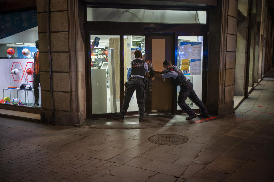 Mossos D'Esquadra, la policía regional de Cataluña, refuerzan la entrada de una tienda que fue saqueada por manifestantes en Barcelona, España, el domingo 1 de noviembre de 2020. Los policías se despliegan por la ciudad costera en el noroeste de España para disolver fiestas clandestinas y despejar las calles de jóvenes que beben alcohol, vigilando el cumplimiento de un toque de queda nacional declarado por el gobierno para frenar los contagios de coronavirus. (AP Foto/Emilio Morenatti)