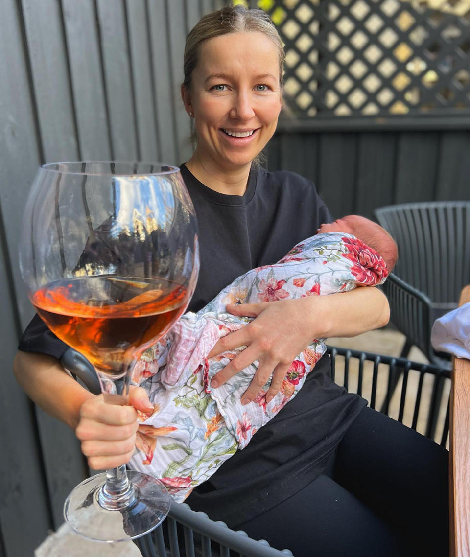 Rebecca James holds a large glass of wine and her newborn baby Margot