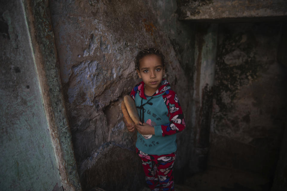 In this in Wednesday, March 25, 2020 photo, a young girl returns with bread she bought for her family in a housing complex in Sale, near Rabat, Morocco. Hundreds of people live in crowded rooms in this Moroccan housing complex with no running water and no income left because of the coronavirus lockdown measures. However volunteers come to help clean as the government tries to protect the population from virus while not punishing the poor. (AP Photo/Mosa'ab Elshamy)