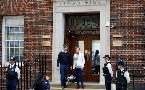 Police officers watch as a couple pose for a photo while holding a baby outside the Lindo Wing - Credit: HENRY NICHOLLS /Reuters