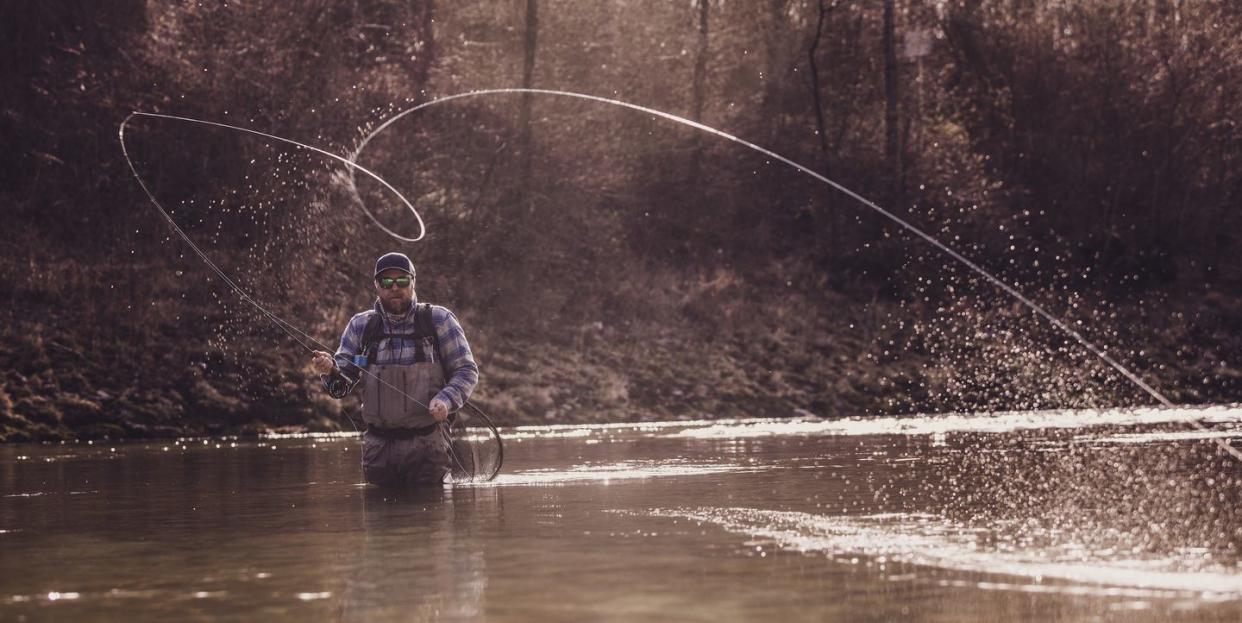 mid adult man throwing fishing reel in river to catch fish during sunset