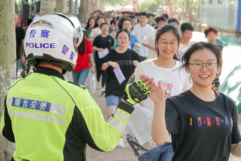 A traffic police officer high fives students as they arrive for the first day of the National College Entrance Examination (NCEE), known as "gaokao", in Yantai, in China's eastern Shandong province on June 7, 2023.