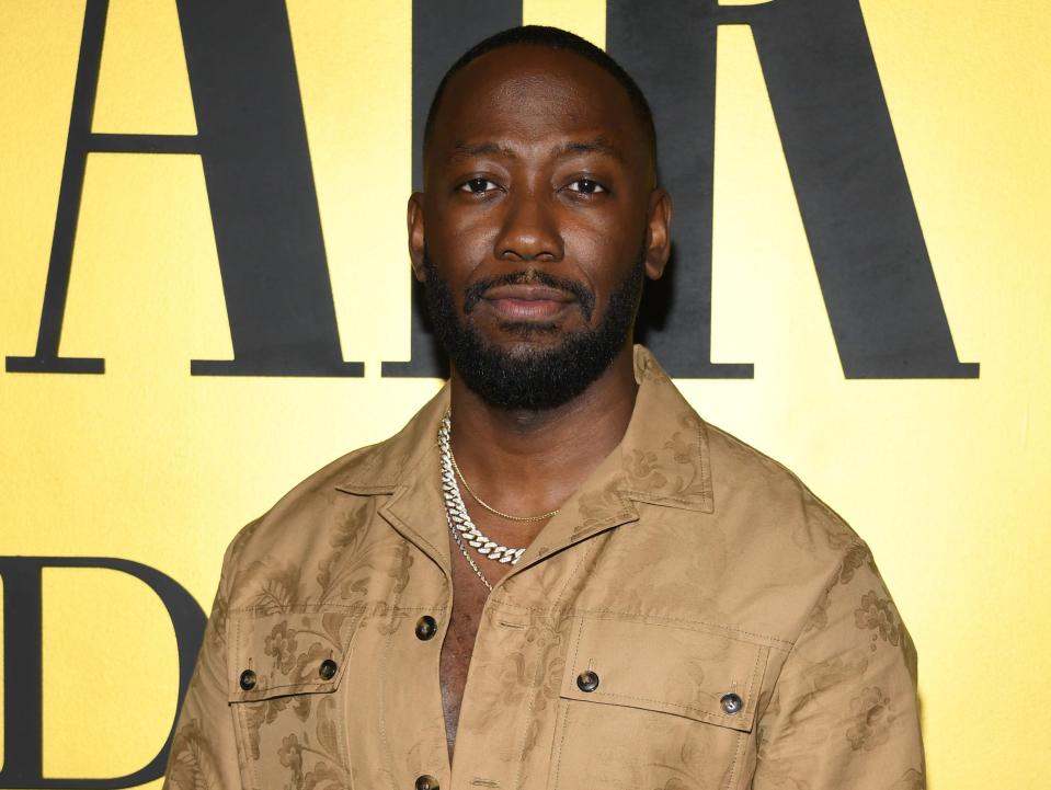 Lamorne Morris in a brown jumpsuit and silver chain in front of gold background