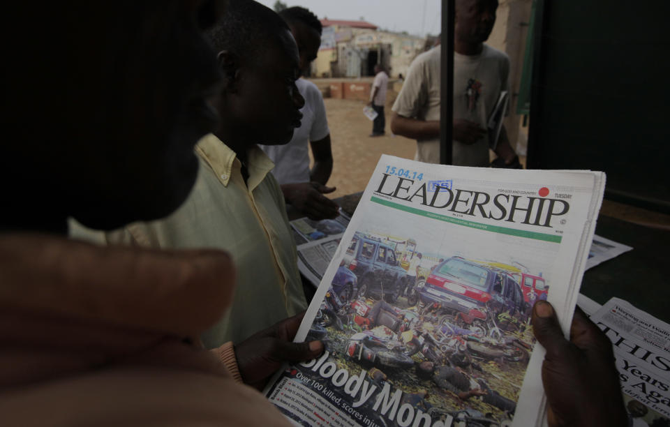 A man reads a local newspaper with headline ''Bloody Monday'' close to the bus park that was bombed just hours before in Abuja, Nigeria, Tuesday, April. 15, 2014, with at least 72 feared dead as the blast destroyed more than 30 vehicles and caused secondary explosions as their fuel tanks exploded and burned. The attack just miles from Nigeria's seat of government increases doubts about the military's ability to contain an Islamic uprising that is dividing the country on religious lines as never before. (AP Photo/ Sunday Alamba)