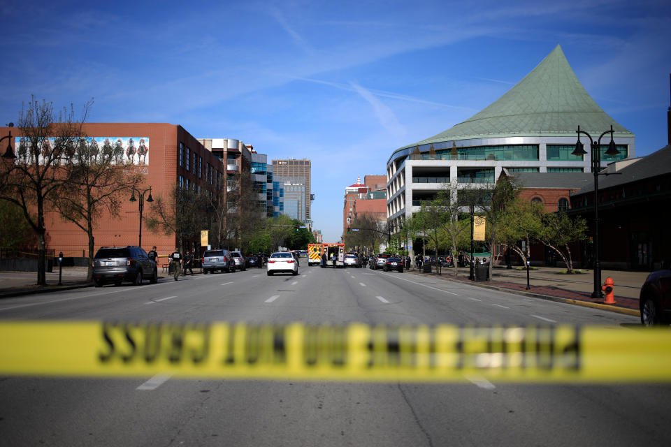 A street is cordoned off with crime scene tape, and emergency vehicles can be seen in the distance.