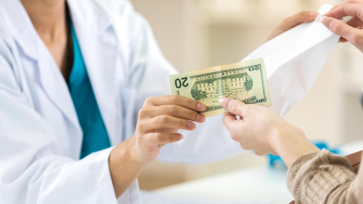 Unrecognizable female pharmacy customer hands pharmacy employee a twenty dollar bill to pay for prescription medication.