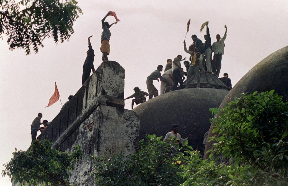 A silhouette of people on top of a old dome like structure, holding saffron flags.