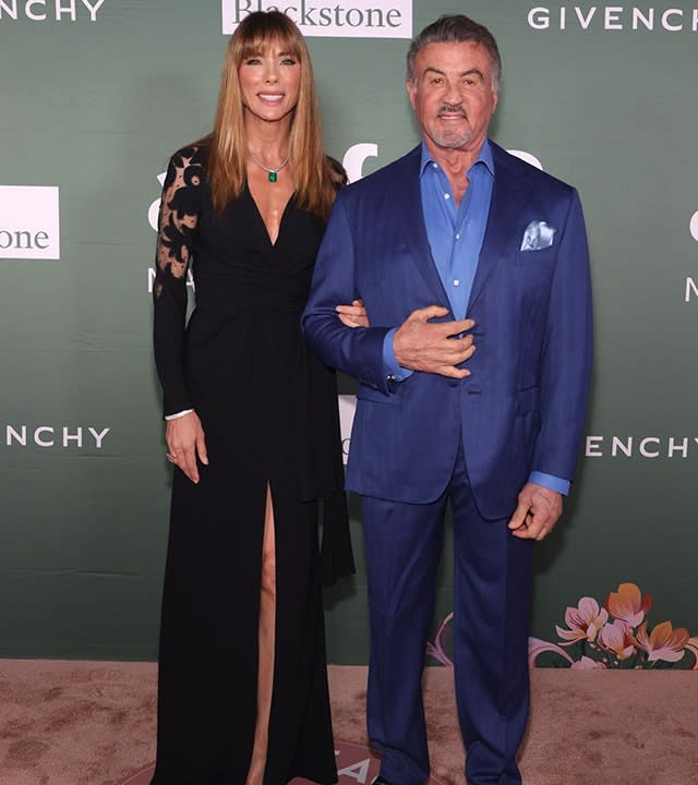 Jennifer Flavin in a black dress with a slit down the middle poses with husband Sylvester Stallone in a bright royal blue jacket