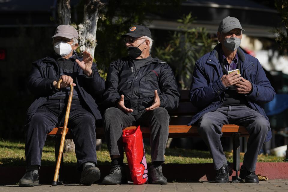 FILE - Three elderly men wearing FFP2 face masks to curb the spread of coronavirus, sit on a bench in Athens, Greece, Monday, Jan. 3, 2022. Italy, Spain and other European countries are re-instating or stiffening mask mandates as their hospitals struggle with mounting numbers of COVID-19 patients. (AP Photo/Thanassis Stavrakis, File)