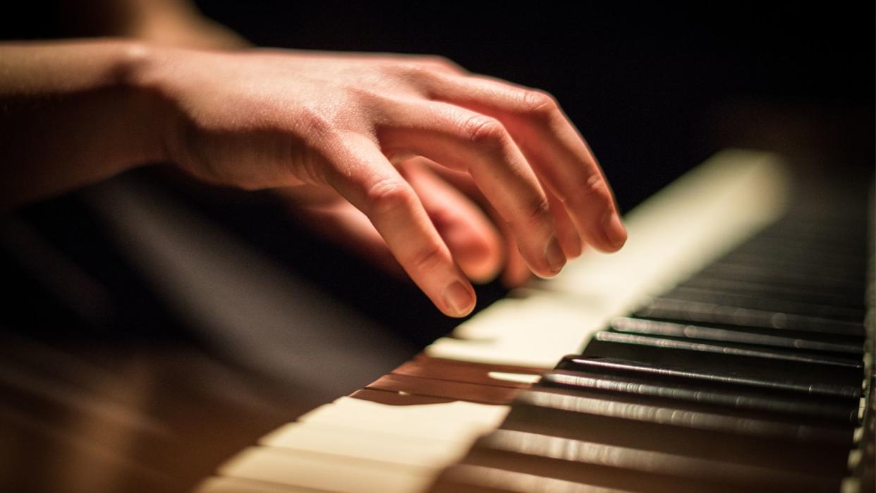  close up of a hand hovering over piano keys, as if to play them 