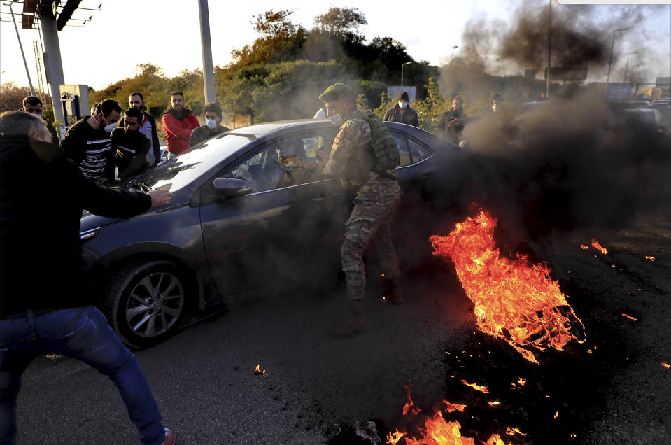 A Lebanese soldier asks a driver to move away from burning tires that were set on fire by protesters to block a highway that leads to Beirut's international airport, in Beirut, Lebanon, Tuesday, March 2, 2021. Scattered protests broke out in different parts of Lebanon Tuesday after the Lebanese pound hit a record low against the dollar on the black market, a sign of the country's multiple crises deepening with no prospects for a new Cabinet in the near future. (AP Photo/Hussein Malla)