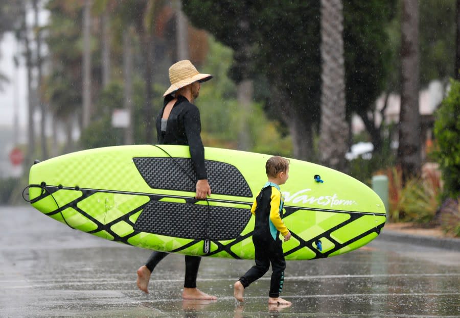 Chad Hilton and his son, Silas, walk back to their place after trying to paddle board at La Jolla Shores as Tropical Storm Hilary arrived on Sunday, Aug. 20, 2023, in San Diego. (K.C. Alfred/The San Diego Union-Tribune via AP)