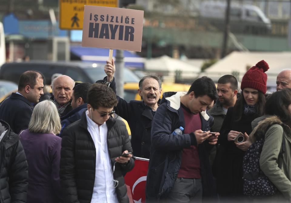 In this Wednesday, March 15, 2017 photo, a Turkish man supporting the 'NO' vote for the upcoming referendum holds a Turkish flag and a placard, reading in Turkish: 'No to unemployment ', as he chants slogans in central Istanbul. The entire Turkish referendum campaign has been biased and unfair, those opposed to expanding the president’s powers say, noting they have been hampered by a lack of TV airtime, threats, violence, arbitrary detentions and even sabotage. Those reports come even as Turkish President Recep Tayyip Erdogan himself has slammed European countries for not letting his ministers campaign on their soil for the April 16 vote on expanding his powers. (AP Photo/Lefteris Pitarakis)