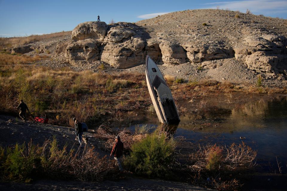 People walk by a formerly sunken boat standing upright into the air with its stern buried in the mud along the shoreline of Lake Mead at the Lake Mead National Recreation Area, Friday, Jan. 27, 2023, near Boulder City, Nev. Six western states that rely on water from the Colorado River have agreed on a plan to dramatically cut use, primarily by California. California, the state with the largest allocation of water from the river, proposed its own plan on Tuesday.